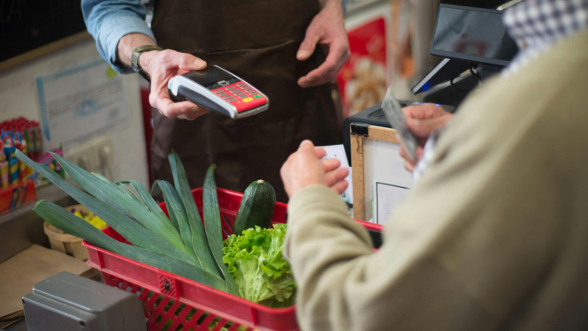 Cilvēks ar iepirkumu grozu pie veikala kases