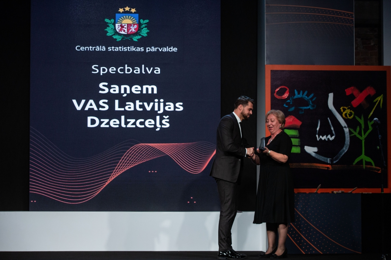 CSP priekšniece Aija Žīgure pasniedz ikgadējo speciālbalvu. VAS “Latvijas Dzelzceļš” saņēmēja lomā iejūtas vakara vadītājs Aivis Ceriņš.