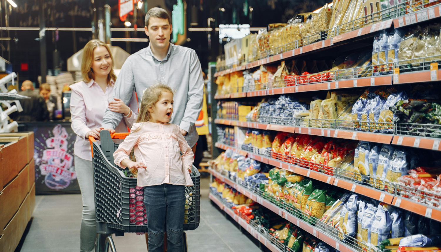 Sieviete, vīrietis un bērns ar iepirkuma ratiem satigā pa lielvaikalu.